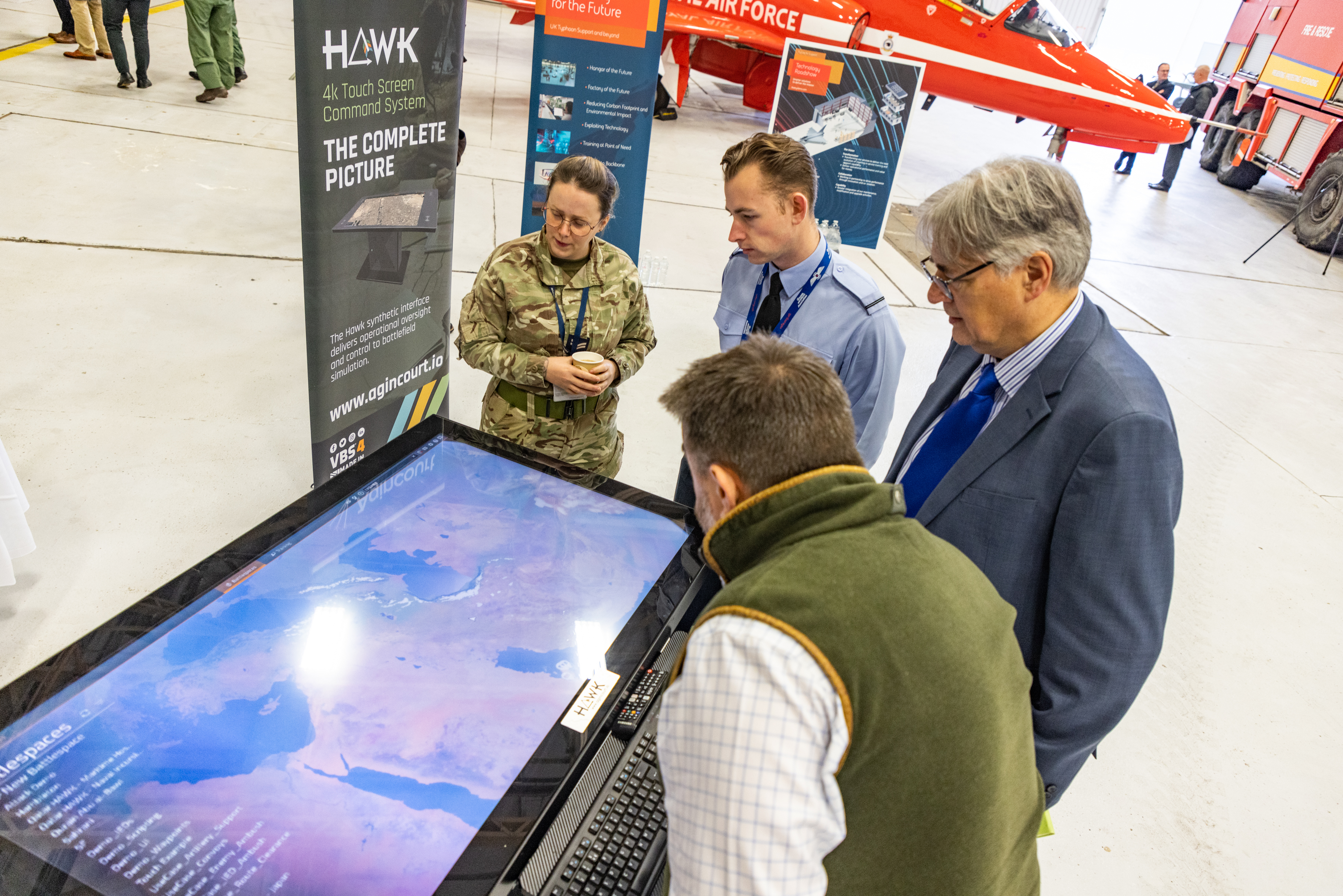 Image shows personnel and civilians looking at a digital screen in a RAF Museum.